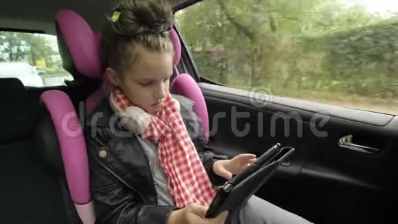 带耳机的青少年女孩坐在汽车座椅上在骑车时使用数码平板电脑视频的预览图
