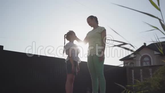 站在后院亲吻妈妈的小可爱女孩女人在孩子面前拍拍的头视频的预览图