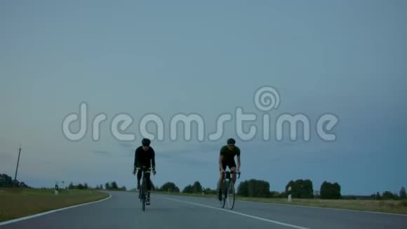 傍晚日落后两个骑自行车的人骑在路上清晨训练骑自行车的人戴头盔视频的预览图