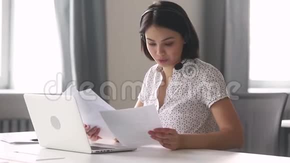 微笑着的亚洲商界女性戴着耳机一边说话一边看着笔记本电脑视频的预览图