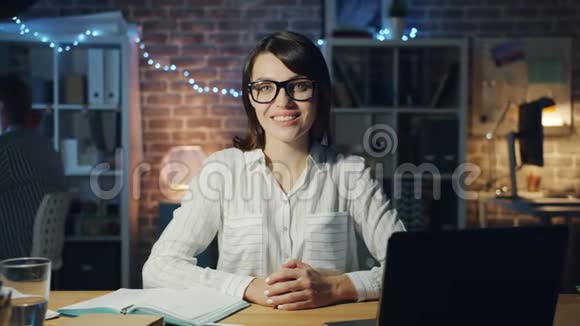 一位漂亮的商务小姐在办公室里晚上坐在办公桌前微笑动作缓慢视频的预览图