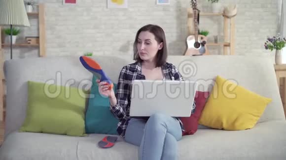 坐在沙发上的年轻女子用笔记本电脑手里拿着矫形鞋垫视频的预览图