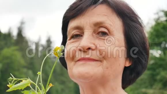 一位年长妇女的户外肖像手里拿着黄色的花享受大自然新鲜空气黄色的花朵和视频的预览图