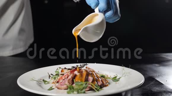 专业厨师蓝手套在餐厅厨房烹饪男人用烤制的手浇上美味的酱汁视频的预览图