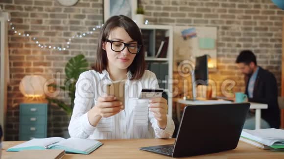 快乐的女人在办公室用智能手机用信用卡在线购物视频的预览图