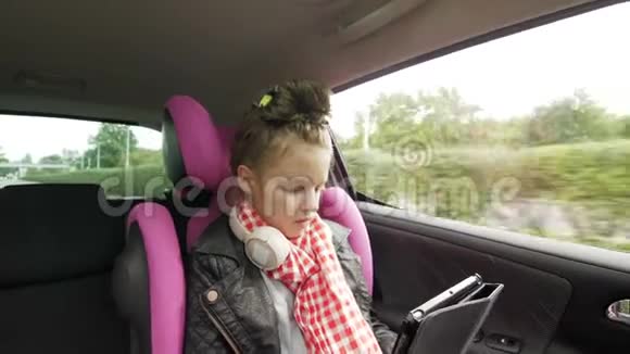 带耳机的青少年女孩坐在汽车座椅上在骑车时使用数码平板电脑视频的预览图