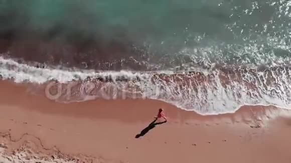 迷人的女人在海滩散步年轻女孩沿着沙滩散步沙滩的鸟瞰图穿红裙子的女孩视频的预览图