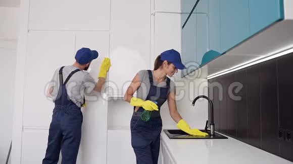 清洁办公室的一对漂亮的年轻夫妇正在擦拭厨房家具视频的预览图