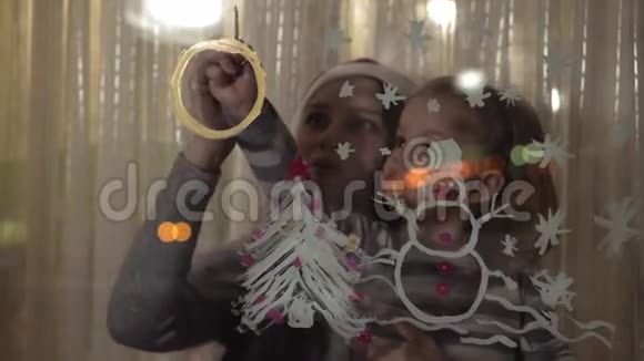 妈妈和女儿在窗玻璃上画一个雪人一棵圣诞树和一个画着颜料的钟上面画着丙烯酸视频的预览图