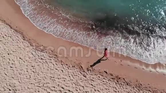 桑迪海岸的小女孩女孩在沙子上留下脚印海滩上穿红色裙子的漂亮女人女孩沿着海滨散步Ae视频的预览图