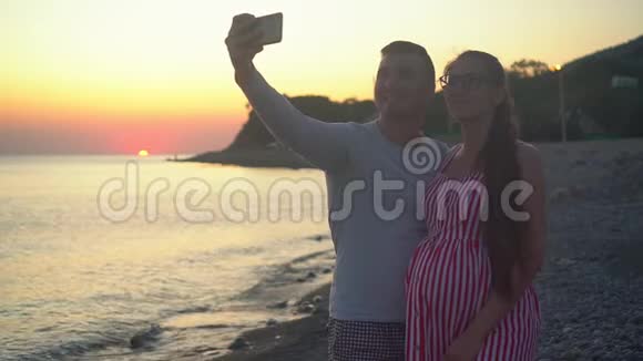 一对年轻的夫妇站在海上日落的背景上一男一女正在自拍视频的预览图