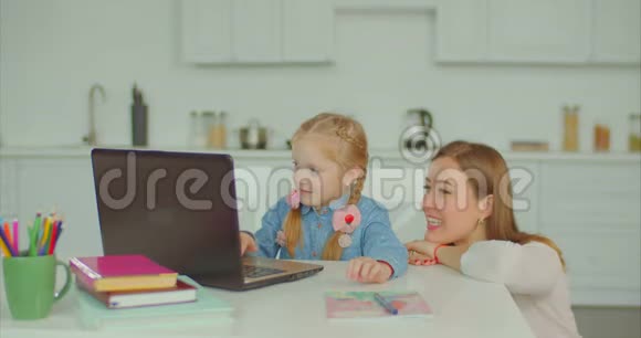 可爱的女孩带着笔记本电脑在妈妈帮助下学习视频的预览图