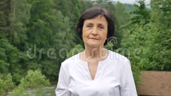 特写一位年长妇女的肖像她留着一头乌黑的短发满脸皱纹微笑着看着山上的摄像机视频的预览图