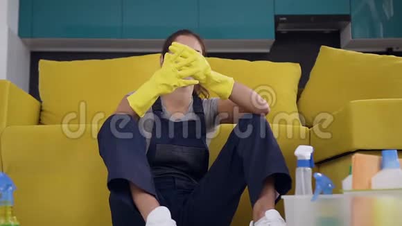 精疲力竭的清洁工人坐在厨房沙发附近脱下橡胶手套把洗涤剂放进盒子里视频的预览图