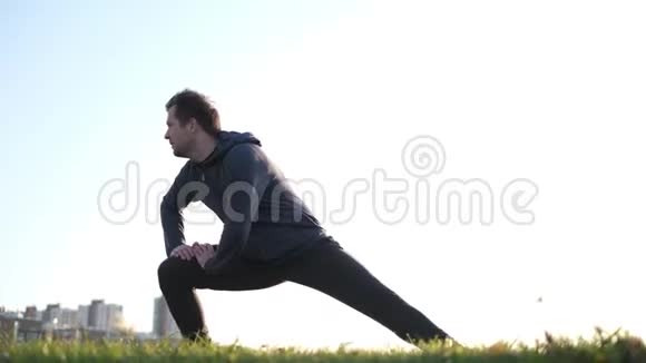 年轻的白种人男运动员在公园里伸腿视频的预览图