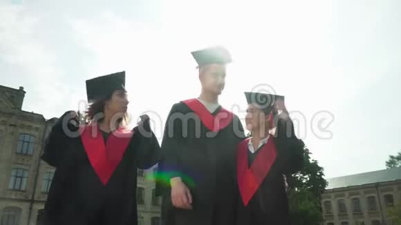 三名学生在大学大楼前庆祝毕业两个女孩和一个男孩出现拇指视频的预览图