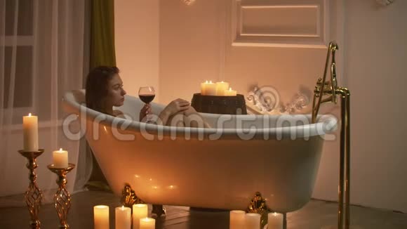 女人躺在泡泡浴中用蜡烛的光放松和喝葡萄酒浪漫的放松芳香疗法视频的预览图