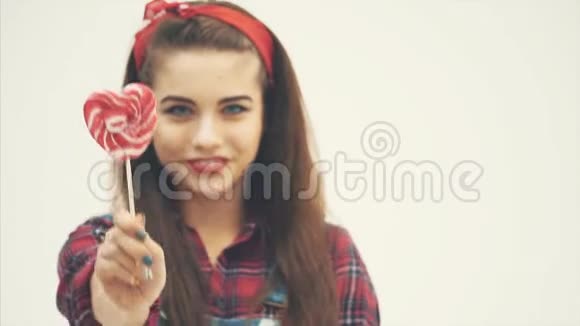 模糊可爱的迷人女孩拿着红色的心形棒棒糖在棍子上在镜头前挥手视频的预览图