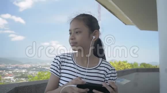 夏天亚洲小女孩用耳机听手机音乐悠闲地在观景塔上散步视频的预览图