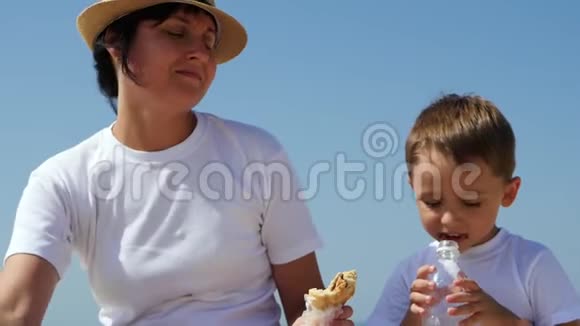 妈妈在沙滩上给孩子喂汉堡包孩子吃汉堡喝塑料水视频的预览图