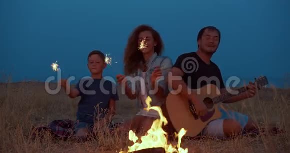 快乐的露营者全家围绕燃烧篝火手持火花微笑旅游休闲视频的预览图