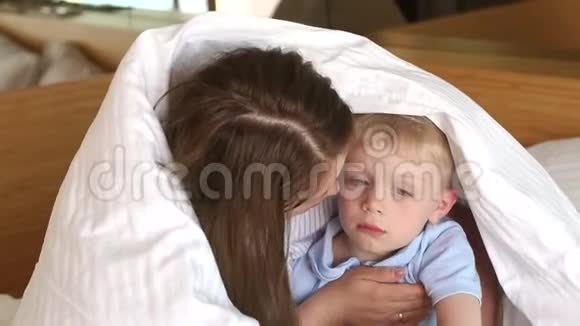 妈妈把她伤心的小儿子抱在毯子下面的床上视频的预览图