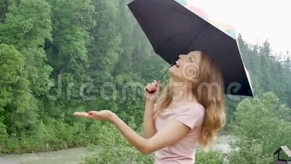 幸福美丽的年轻女子带着雨伞在春雨下女孩穿着粉红色的裙子享受着降雨视频的预览图