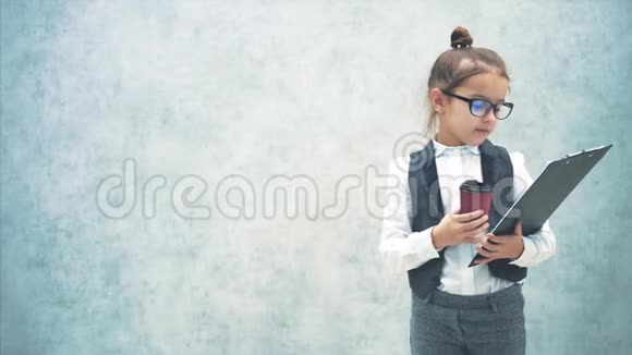 那个小女孩的背景是灰色的在此期间它从一个黑色文件夹中读取信息并喝咖啡视频的预览图