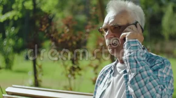 一位英俊的老人在公园的长凳上打电话视频的预览图
