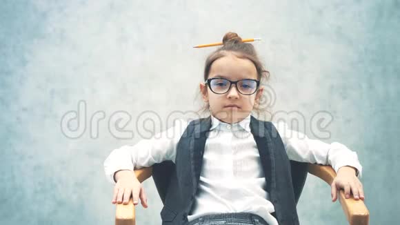 一个小商业女孩坐在灰色背景的椅子上的特写在这段时间里厌倦了躺在床上视频的预览图