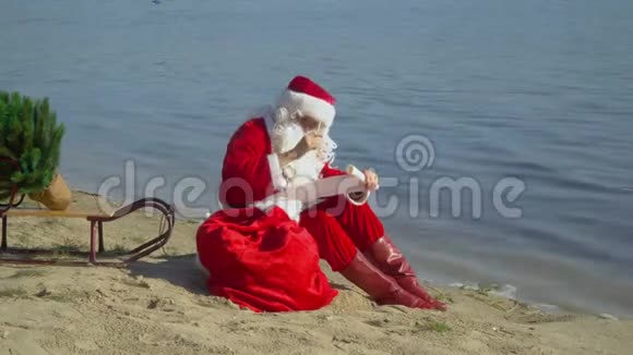 圣诞老人坐在湖边的沙滩上手里拿着一袋礼物犹豫了之后他把一些东西写在清单上视频的预览图