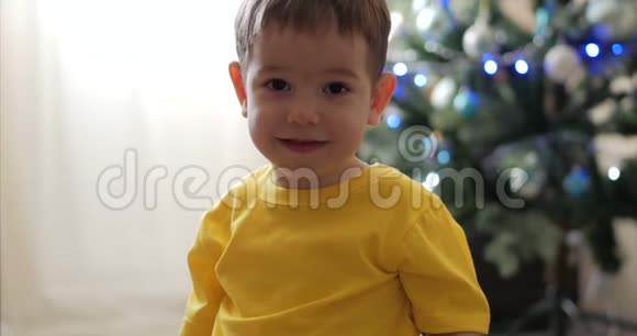有趣的小男孩在圣诞灯的背景上微笑可爱的宝宝看着相机微笑着快乐着快乐视频的预览图