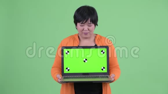 快乐年轻的超重亚洲女人一边思考一边展示笔记本电脑准备健身房视频的预览图