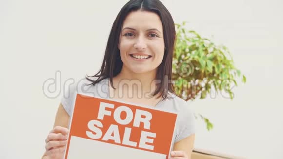 微笑的年轻美丽的女人拿着一个盘子上面写着出售的文字放弃了拇指视频的预览图