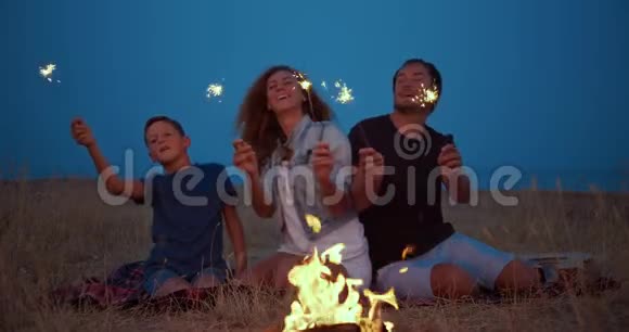 快乐的露营者全家围绕燃烧篝火手持火花微笑旅游休闲视频的预览图
