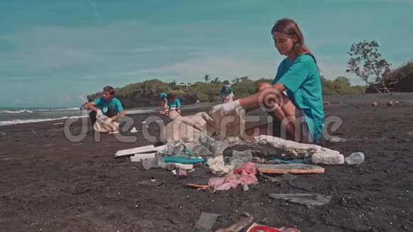 穿蓝色T恤的年轻女性和朋友在海滩上收集垃圾桶视频的预览图