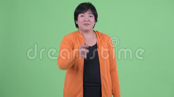 快乐年轻超重的亚洲女人指着相机准备健身房视频的预览图
