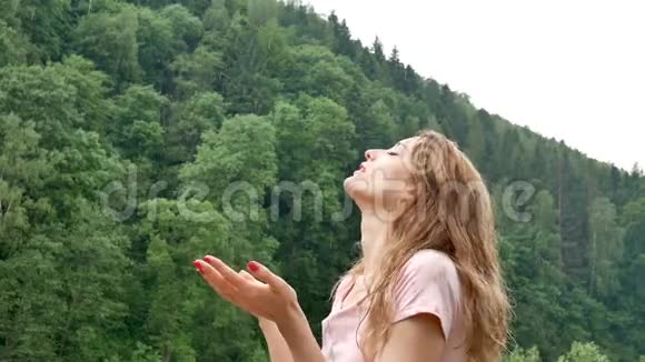 一位金发碧眼的年轻女士在没有雨伞的雨天带着绿色森林的山上在户外做红色指甲视频的预览图