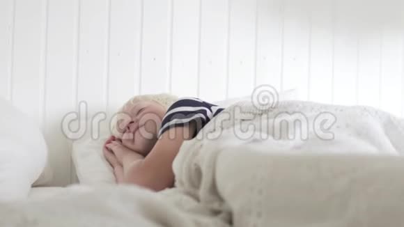 可爱的男孩在一张白色的床上醒来啜饮着视频的预览图