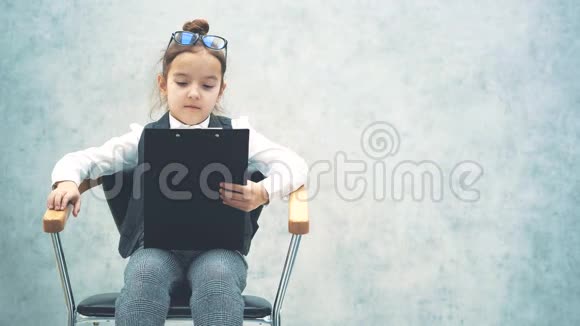 一个小老板坐在椅子上手里拿着一个黑色的文件夹灰色背景特写仔细阅读视频的预览图