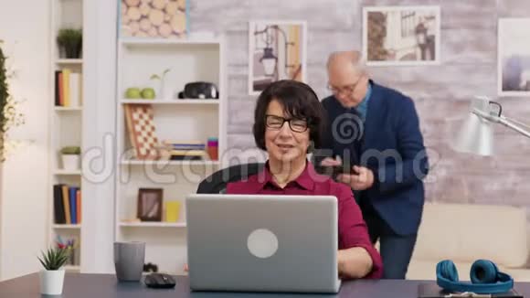 兴奋的老妇人在客厅里用笔记本电脑视频的预览图