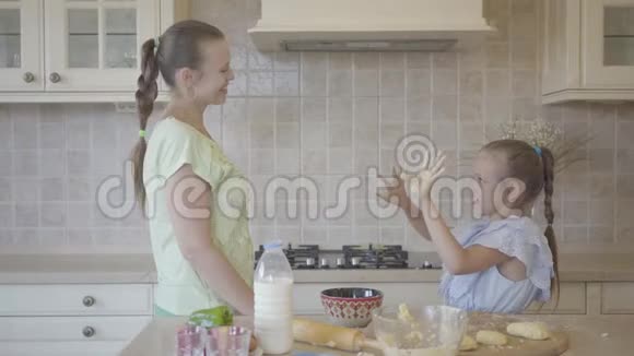 肖像年轻女子和她的小女儿在家厨房里做蛋糕女孩抚摸着妈妈脸视频的预览图
