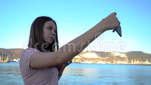 有魅力的年轻女性使用手机在路堤上自拍背景是山脉和多云的天空视频的预览图
