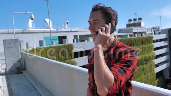 一个穿着格子衬衫的年轻人微笑着在一栋建筑的屋顶上用手机说话背景是视频的预览图