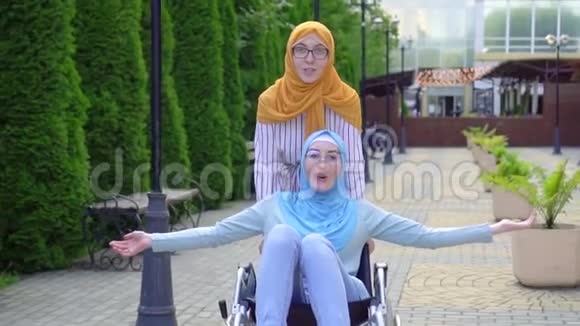 在公园散步时坐在轮椅上的一位积极的残疾青年妇女微笑着伸出双手视频的预览图