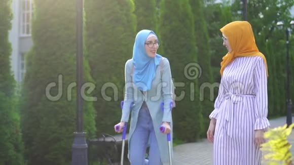 带着微笑的年轻女子在受伤后拄着拐杖与女友在公园散步视频的预览图