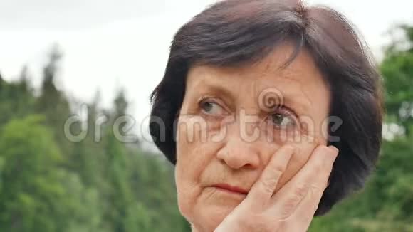 一位留着乌黑短发满脸皱纹想着退休后孤独生活的老年妇女的户外肖像画视频的预览图
