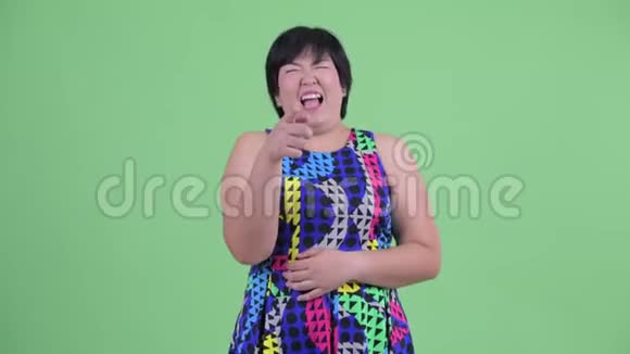快乐的年轻超重的亚洲女人笑着指着相机准备聚会视频的预览图