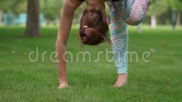 一个女孩在草地上慢动作地训练一个困难的瑜伽姿势视频的预览图