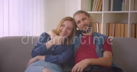 一对年轻夫妇在电视上看喜剧电影在家开心地笑着视频的预览图